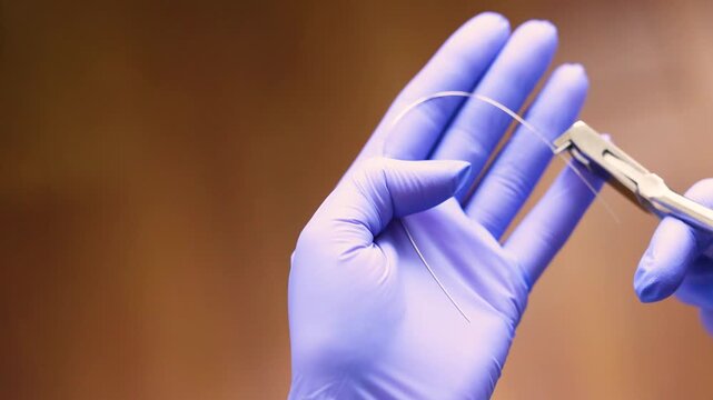 Dentist hands handling orthodontic ligature wire with needleholder instrument for braces adjustment