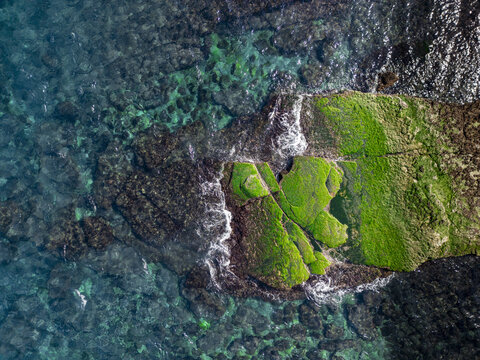 Aerial view of a vibrant green algae-covered rock formation contrasting against the clear turquoise water, creating a striking visual harmony, Aquaculture, New Taipei City, Taiwan.