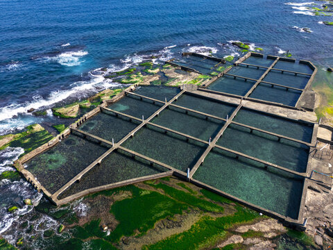 Aerial view of the geometric aquaculture ponds contrasting beautifully with the rugged coastline and deep blue sea, creating a stunning visual harmony, Aquaculture, New Taipei City, Taiwan.
