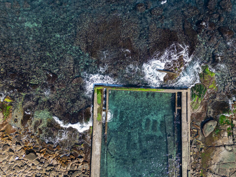 Aerial view of the turquoise aquaculture pond contrasts with the dark, rocky shoreline, creating a stunning visual spectacle, Aquaculture, New Taipei City, Taiwan.