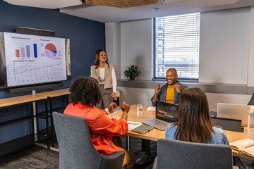 Diverse coworkers presenting and discussing charts on large monitor in conference room with laptops