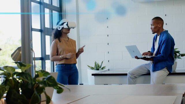 Woman using VR headset starting tech demo, gesturing blue UI while man checking laptop for review