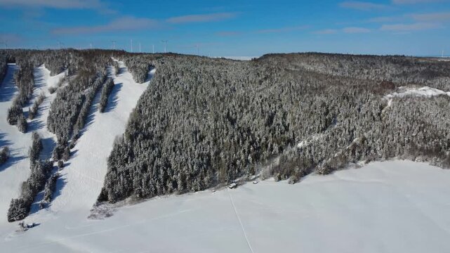 Aerial view of a mountain with its ski slopes and alpine ski runs on the side of a freshly snow-covered mountain with wind turbines at its summit. Mont-Castor, Matane, Gasp&eacute; Peninsula, Quebec, Canada,