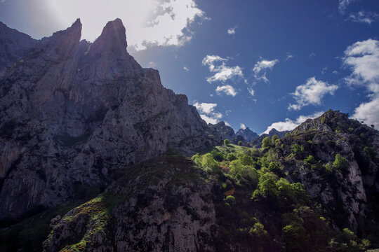 Cumbres rocosas escarpadas y laderas verdes bajo un cielo azul brillante.