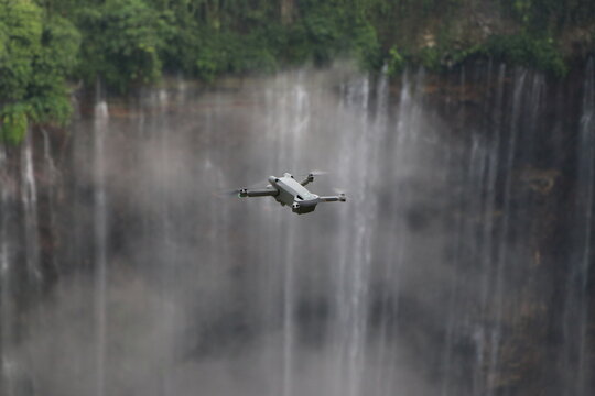 Aerial view of a drone soaring near a powerful waterfall cascading down a verdant cliff, mist rising to meet the lush canopy, Java, Indonesia.