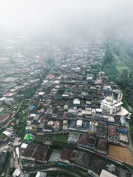 Aerial view of a densely packed village nestles amidst the misty hills, with a prominent mosque standing out against the landscape, Java, Java, Indonesia.