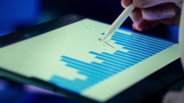 Bar chart data visualization tablet stylus closeup. Designer hand marking upward arrow digital screen horizontal bars soft focus background cool blue lighting modern studio workspace