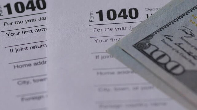 US Individual Income Tax Return form 1040 with stack of hundred dollar bills. Concept of tax payment, refund and financial accounting