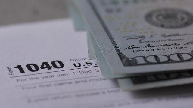 Close up of US Individual Income Tax Return Form 1040 with counting hundred dollar bills. Financial concept of tax payment, IRS refund and annual accounting reporting