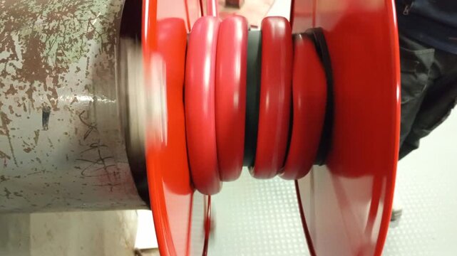 Detailed view of red industrial fire hose rolling onto a spool mechanism"