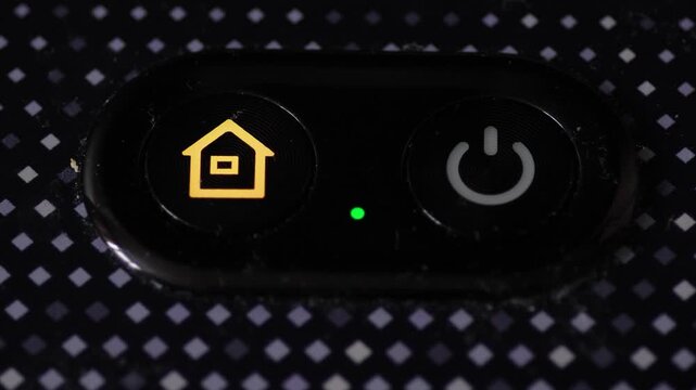 Macro shot of a control panel with power and home buttons on a black textured surface. Green LED indicator light signaling the operation of a smart home device