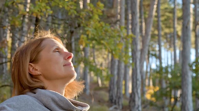 Woman breathing fresh air in spring forest at sunset. The air in the coniferous forest reduces cortisol levels, improves mental health and connects the soul to the environment.
