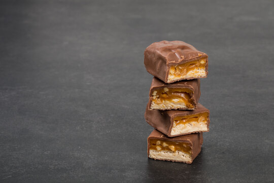 Chocolate bar with nougat and caramel, peanuts and hazelnuts. Close up. Dark background. Copy space