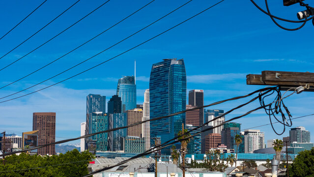 Aerial view of towering skyscrapers punctuate the skyline, their glass facades reflecting the clear blue sky, juxtaposed against the tangled web of power lines, Los Angeles, California, United States.