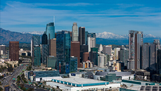 Aerial view of skyscrapers piercing the sky, contrasting against the distant snow-capped mountains, a vibrant urban landscape sprawling below, Los Angeles, California, United States.
