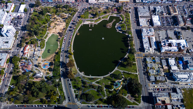 Aerial view of the sprawling green park embracing a dark lake, surrounded by the city's bustling streets and buildings, MacArthur Park, Los Angeles, California, United States.