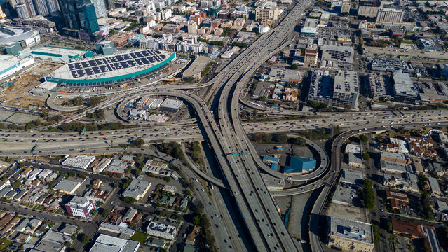 Aerial view of a complex interchange system weaving through the urban landscape, juxtaposed against the Crypto.com Arena and its solar panels, Los Angeles, California, United States.