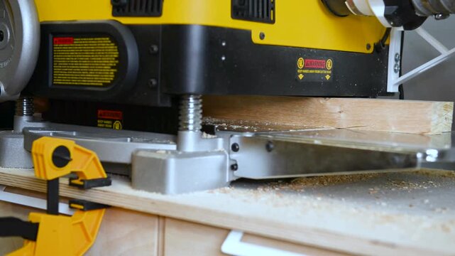 A wood plate passing through the thickness planer machine in a carpentry workshop. Woodworking process, furniture preparation, handmade craftsmanship, carpentry studio.