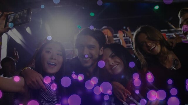 Friends leaning in raising phone, starting group selfie at concert, purple bokeh revealing faces
