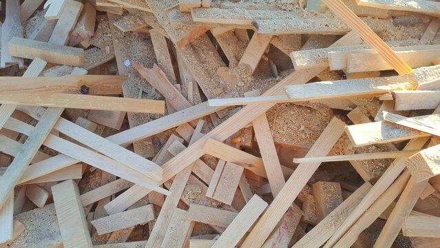 Pile of raw wood scraps and timber offcuts in a carpentry workshop, industrial wooden waste background for recycling and construction industry.