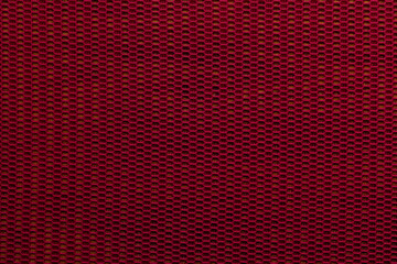 Fototapeta premium Texture of red fabric shows intricate pattern with hexagonal shapes and small openings in a close-up view during daylight hours