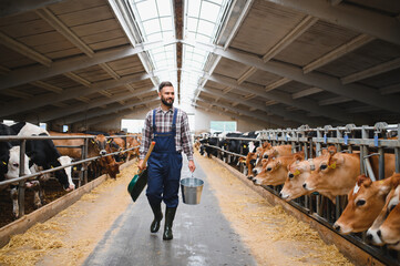 Farmer walking in cowshed carrying shovel and bucket