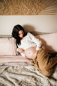 pregnant Mother sitting on bed with baby things
