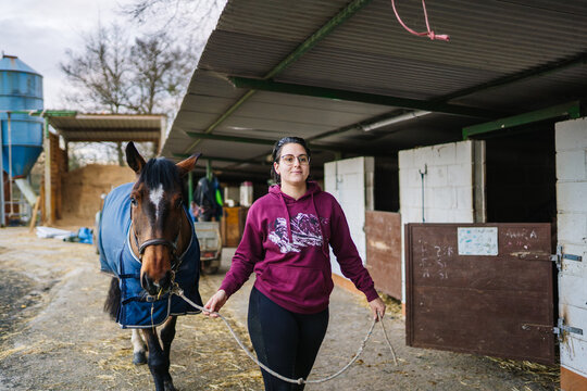 Woman leading horse wearing blanket from stable