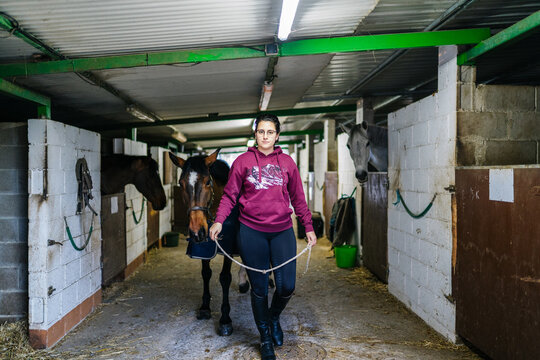 Woman leading horse through stable barn aisle