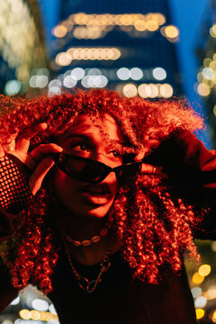 Woman raising sunglasses in urban night glow