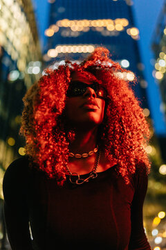 Woman with red curly hair looking up at city night