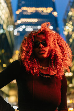 Confident Black woman with red curly hair in city night
