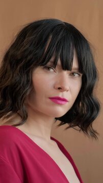 White Woman Portrait In Red Dress, Model, Actress Posing With Wavy Bob Hair Style And Blunt Bangs, Bold Pink Lipstick, Soft Brown Backdrop, Vivid Make-up, Red Lips, Confident. Fashion Beauty Hairstyle