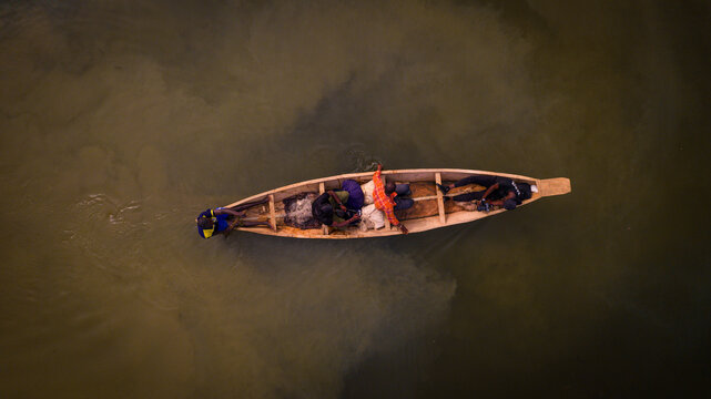 Aerial view of a solitary canoe slicing through the murky waters near Kofa Dam, a scene of quiet industry and timeless tradition, Suleja, Niger, Nigeria.