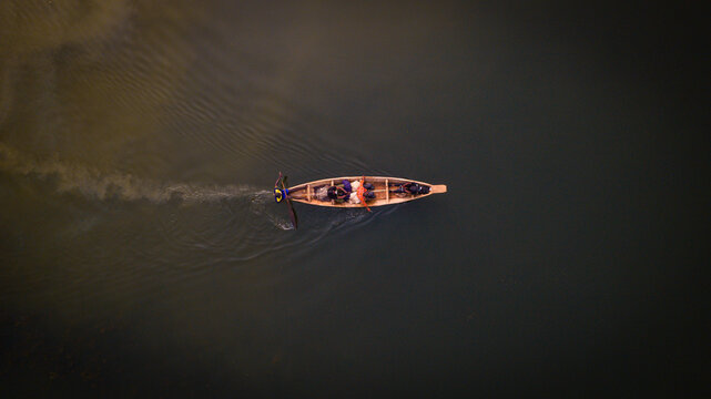 Aerial view of a lone wooden canoe slicing through the still, dark waters of Kofa Dam, leaving a foamy trail in its wake, Suleja, Niger, Nigeria.