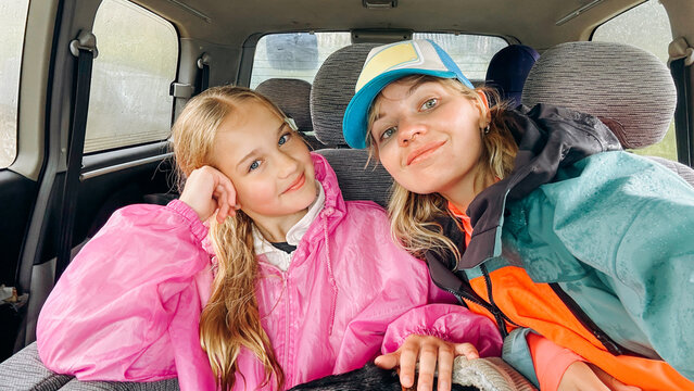 Two young girls relax inside a car during rainy weather