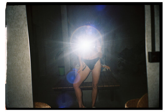 Model poses in front of mirror with flash at night during a photoshoot