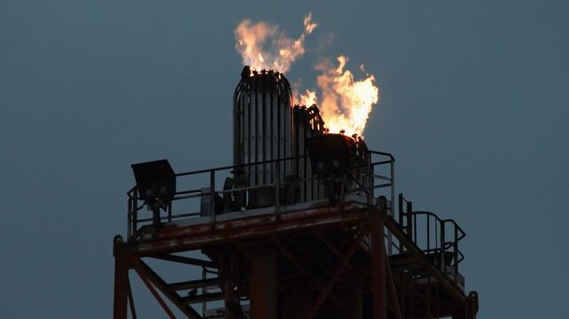 Industrial gas flare burning at petroleum refinery at dusk.  energy production, carbon emissions, and the rising cost of fuel. financial market and oil market volatility. 