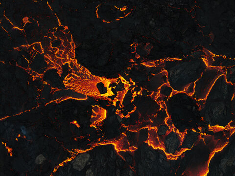 Aerial view of molten lava cascading down rugged, blackened terrain, creating a mesmerizing dance of fire and earth, Iceland.