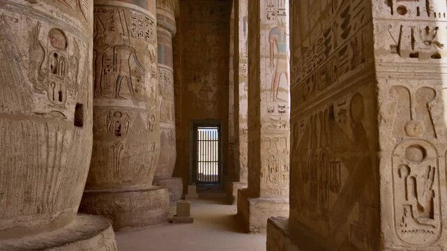 Medinet Habu temple colonnade with hieroglyphic inscriptions and relief carvings in Luxor Egypt, massive sandstone columns with papyrus capitals under dramatic blue sky.