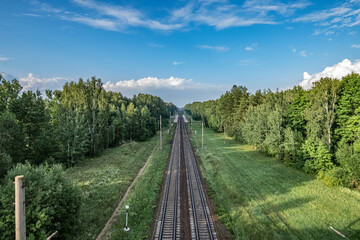 Obraz premium Railway tracks stretching through a green landscape with trees and blue sky, showcasing a serene rural environment in a natural setting