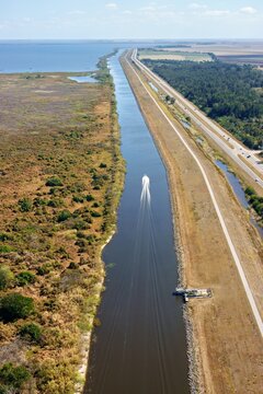 Aerial view of a boat speeding down a narrow canal, flanked by the highway and wetlands, under a clear blue sky, Lake Harbor, Florida, United States.