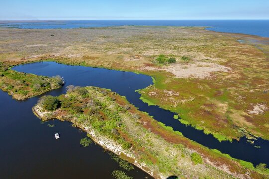 Aerial view of the dark waters winding through the vibrant green and brown landscape near Lake Okeechobee, Lake Harbor, Florida, United States.