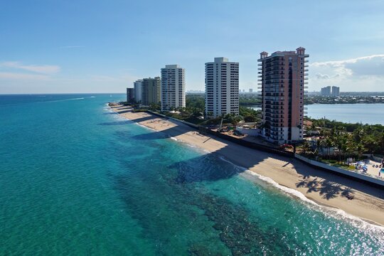 Aerial view of turquoise waters meeting the sandy beach and towering buildings in a vibrant coastal scene, Riviera Beach, Florida, United States.