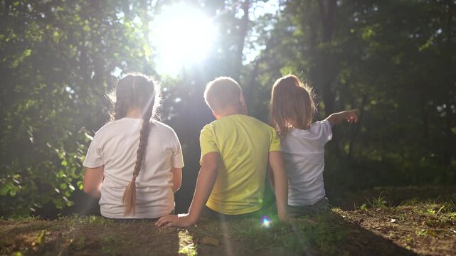 children sit on the banks of the river. happy family childhood dream concept. a group of little children sit together by the river and talk lifestyle. kids spend time outdoors in nature in the forest