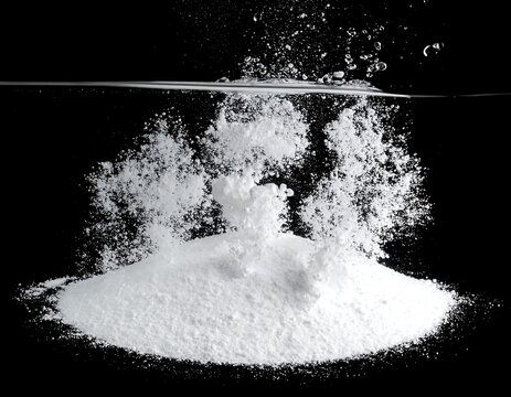 A white powder dissolving in water, creating effervescent bubbles against a stark black background