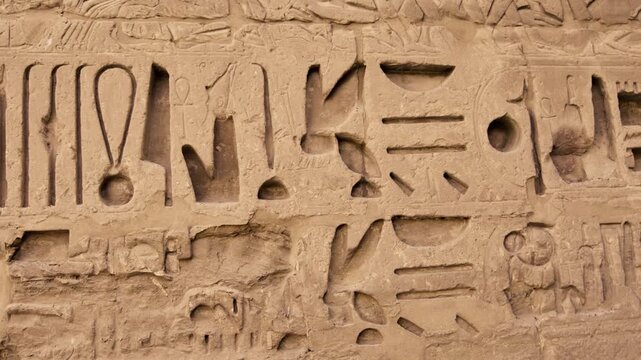 Closeup of ancient Egyptian hieroglyphic inscriptions with cartouches and bird symbols carved in sandstone wall at Medinet Habu temple in Luxor Egypt, detailed royal text.