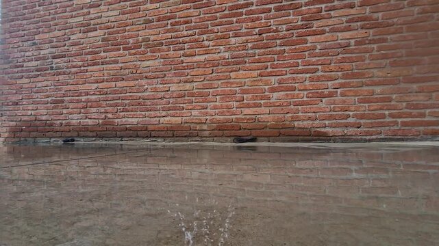 Raindrops falling in a puddle near a brick wall