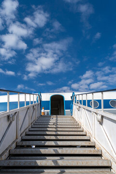Steps lead up to an airplane waiting at the airport under a blue sky and clouds with no visible people around