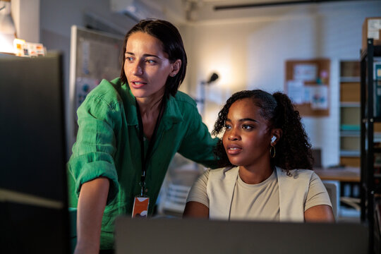 Two women collaborate on a computer in an office.